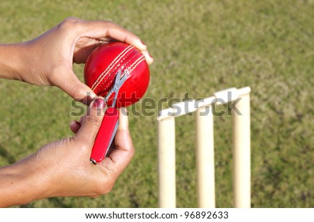 Umpire cutting the ripped thread from a cricket ball