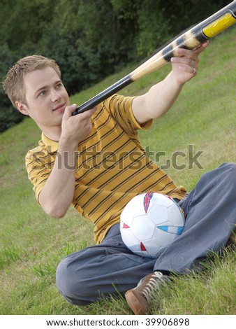A young guy sitting on the grass with a ball and aiming by a bit.