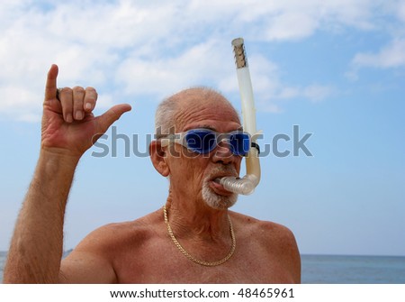 Retired senior man on beach wearing snorkel and dive goggles giving a friendly Shaka wave