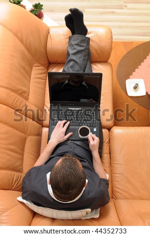 Top view of businessman holding a cup of coffee and working on portable computer on luxurious sofa.