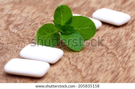 Chewing gum with mint leaves on wooden surface
