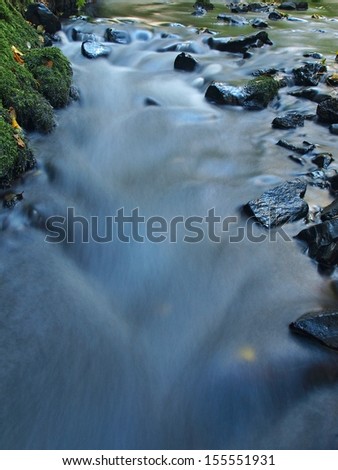 Blurred blue waves of stream running over gravel and stones, reflections in the water level.