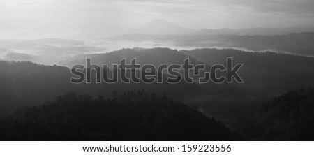 Sunrise in a beautiful mountain of Bohemian-Saxony Switzerland. Sandstone peaks and hills increased from foggy background. First sun rays. Black and White photo.