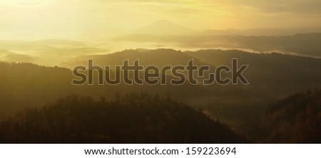 Sunrise in a beautiful mountain of Bohemian-Saxony Switzerland. Sandstone peaks and hills increased from foggy background, the fog is orange due to sun rays.