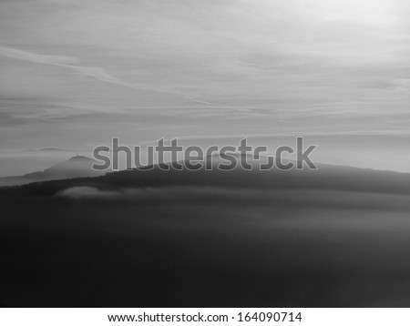 Autumn sunrise in a beautiful mountain of Bohemia. Peaks of hills increased from foggy background. Black and white photo.