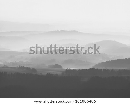Misty daybreak, far hills with old stronghold are sticking out from ground fog. Cold sun rays. Black and white photos.