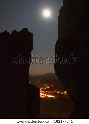 Full moon above rocks, fog is shaking above river and town on river banks.