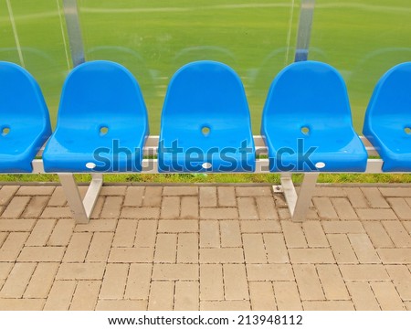 New blue plastic seats on outdoor stadium players bench, chairs with new paint below transparent plastic roof.