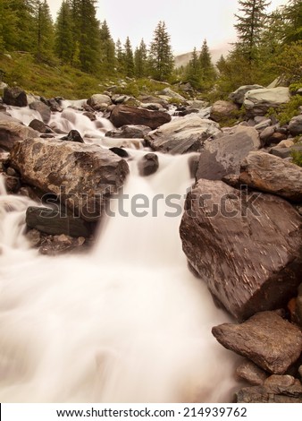 Steep stony stream bed of Alpine brook. Blurred waves of stream running over boulders and stones,  high water level after heavy rains.