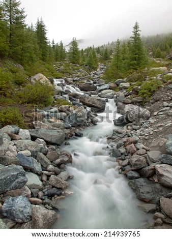 Steep stony stream bed of Alpine brook. Blurred waves of stream running over boulders and stones,  high water level after heavy rains.
