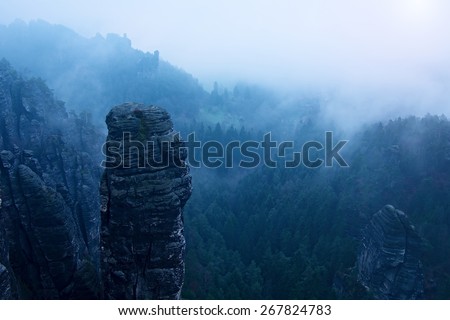 Autumn early morning view over sandstone rocks to fall valley of Saxony Switzerland. Sandstone peaks and hills increased from heavy mist.