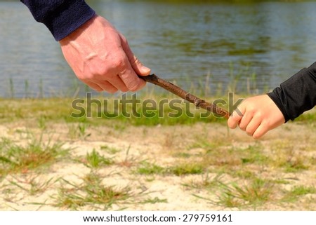 Father\'s large hand pass dry stick to hand of a little boy. Hands in blue and black shirts.