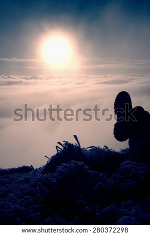Man legs in big boots laying on the ground in a frozen grass, resting on a hill. Tired hiker and watching into misty daybreak. Autumn misty day in mountains.