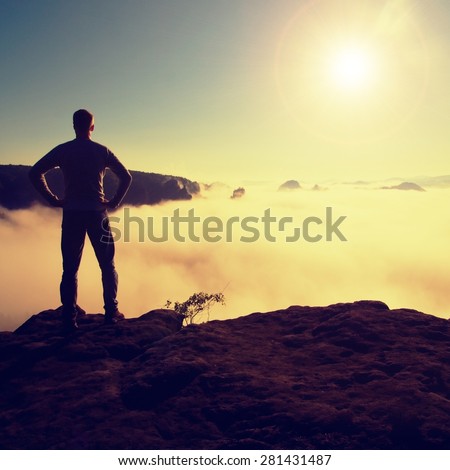 Man in shirt and jeans is standing on the peak of sandstone empire  and watching over the misty and foggy morning valley to Sun. Beautiful moment the miracle of nature