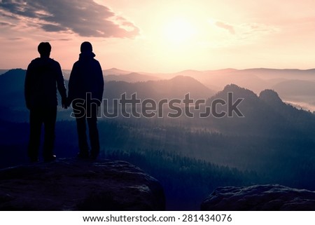 Couple in love enjoying tender moments during sunset .  Young pair of hikers hand in hand on the peak of rock empires park and watch over the misty and foggy morning valley to Sun.