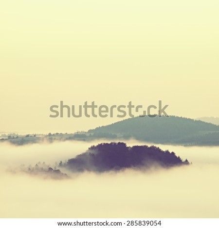 Misty sunrise above a valley. Sandstone peaks increased from fog, the fog is colored to blue, gold and orange.
