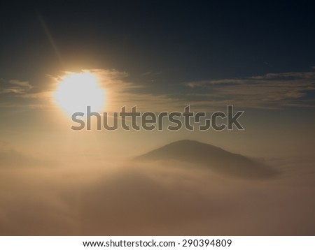 Heavy mist in landscape. Autumn fogy sunrise in a countryside. Hill increased from fog, the fog is colored to golden and orange.