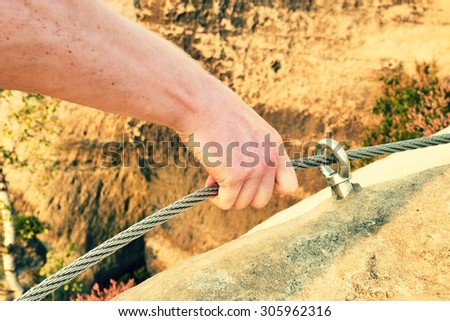 Rock climber\'s hand hold on steel twisted rope at steel bolt eye anchored in sandstone rock. Tourist path via ferrata.