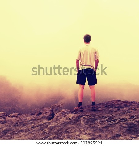 Man in shirt and pants. Tourist on the peak of sandstone rock into misty landscape.