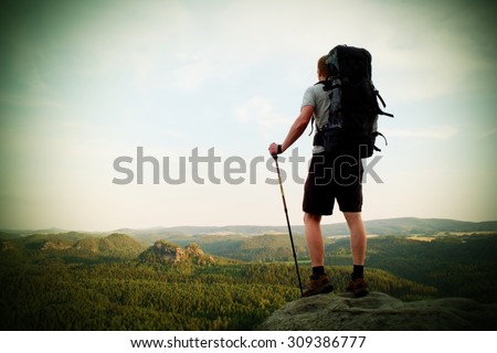Tall tourist with poles in hand. Sunny evening in rocky mountains. Hiker with big backpack stand on rocky view point above misty valley.  Vignetting effect.