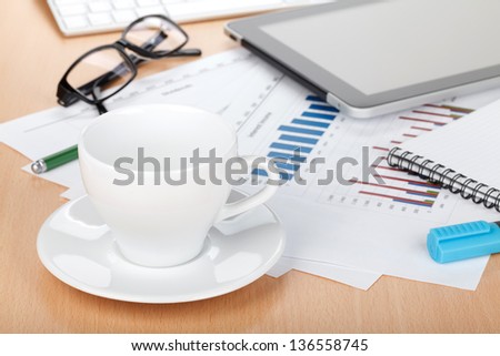 Coffee cup on contemporary workplace with financial papers, computer, glasses and office supplies