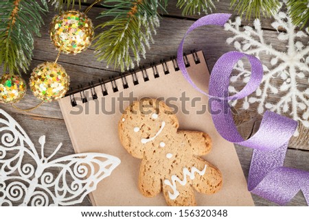 Christmas fir tree covered with snow, decor and blank notepad on wooden board background