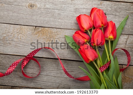 Fresh red tulips with ribbon over wooden background with copy space
