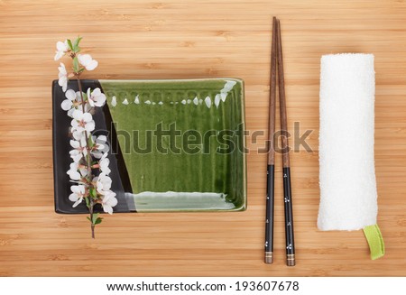 Empty plate, chopsticks and sakura branch over bamboo table