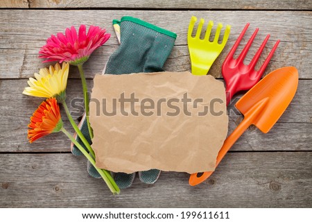 Gardening tools and colorful flowers and paper for copy space on wooden table background