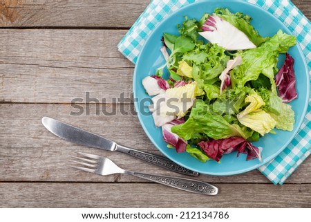 Plate with fresh salad, knife and fork. Diet food on wooden table with copy space