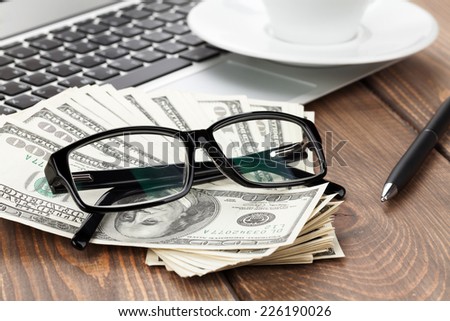 Office table with pc, coffee cup and glasses over money cash closeup