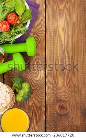 Dumbells, tape measure and healthy food over wooden background. Fitness and health. View from above