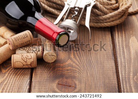 Red wine bottle, heap of corks and corkscrew over rustic wooden table background with copy space