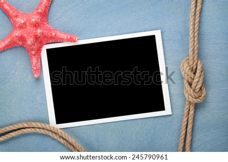 Blank photo frame with starfish and ship rope over blue wooden background