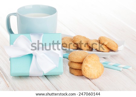 Cup of milk, heart shaped cookies and gift box on white wooden table
