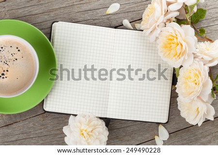 Blank notepad, coffee cup and white rose flowers on wooden table background