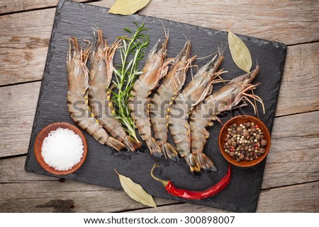 Fresh raw tiger prawns and spices on  black stone plate over wooden table