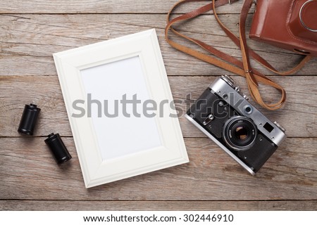 Vintage film camera and blank photo frame on wooden table. Top view