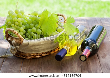 White and red wine bottles, vine and bunch of grapes on garden table