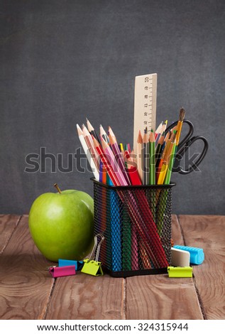School and office supplies and apple on classroom table in front of blackboard