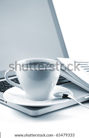 Hot cappuccino cup on laptop and newspaper. Blue toned