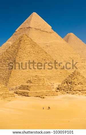 A camel riding tourist passes the base of Great Pyramids in Giza showing the relative scale of the structures in Cairo, Egypt