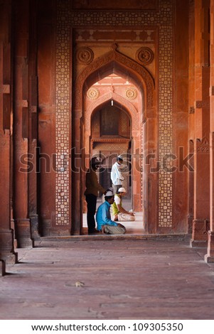 FATEPHUR SIKRI, INDIA - NOVEMBER 18,: Muslims pray inside the doorway of the fort mosque, a famous tourist attraction, for afternoon prayers on November 18, 2009 in Fatephur Sikir, India