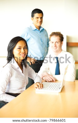 A diverse group of attractive business people smile during a meeting using a laptop led by a beautiful businesswoman.