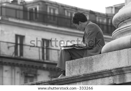 Man sitting at the base of a pillar reading a newspaper in Paris, France,