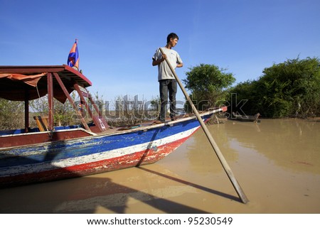 SIEM REAP, CAMBODIA-JAN 21: Cambodian man pushes his boat in mud on Tonle Sap Lake in Siem Reap, Cambodia on January 21, 2012. Tonle Sap is the largest freshwater lake in SE Asia peaking at 16k km2