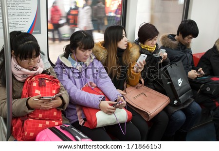BEIJING, CHINA-JAN. 11,2014: Passengers use their mobile phones in a subway train. Mobile phones and tablets are used for people to entertain and view information when they take public transportation.
