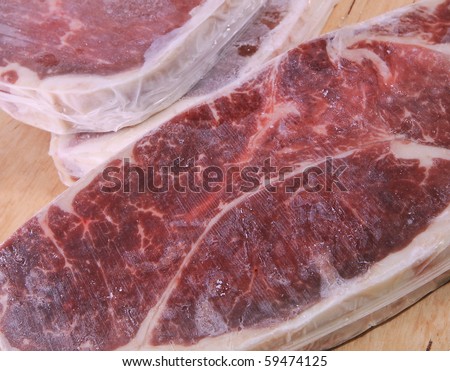 Frozen food. Three pieces of frozen strip loin steak on a wooden table