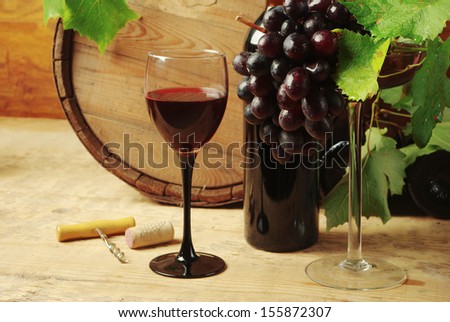 Still life with wine bottles, one glass of red wine, grapes  and oak barrel