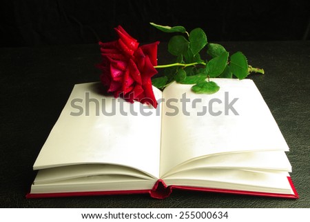 Book and red rose on black